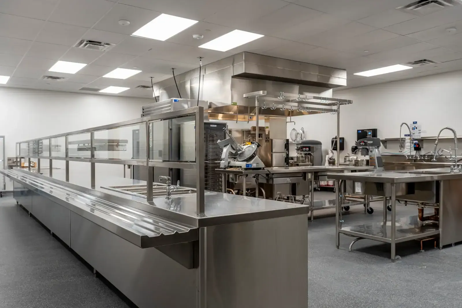 Kitchen with a stainless steel serving line, a slicer, a mixer and a ventilation hood.