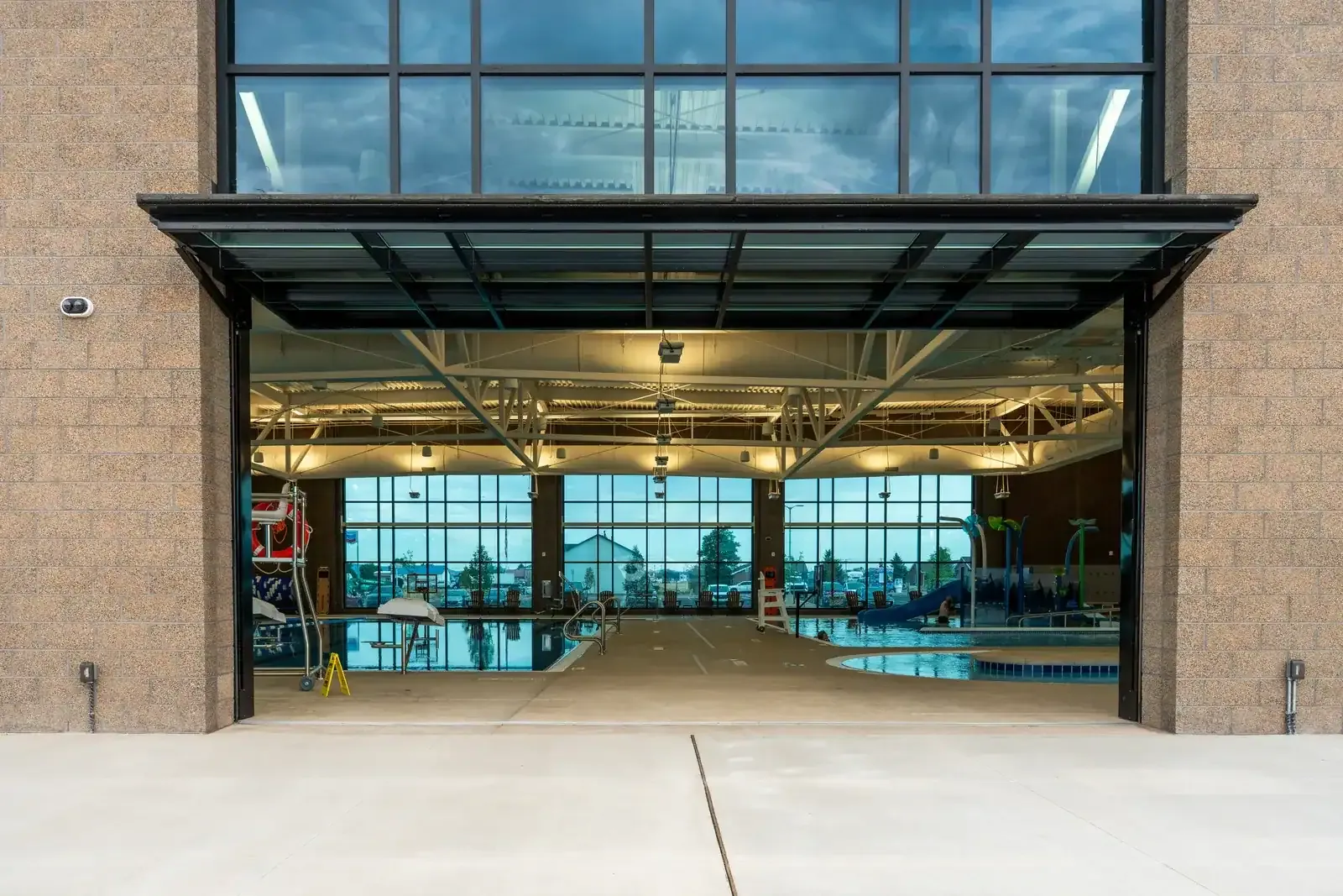 Open overhead door in the building's exterior wall, with the indoor pool and a slide visible inside.