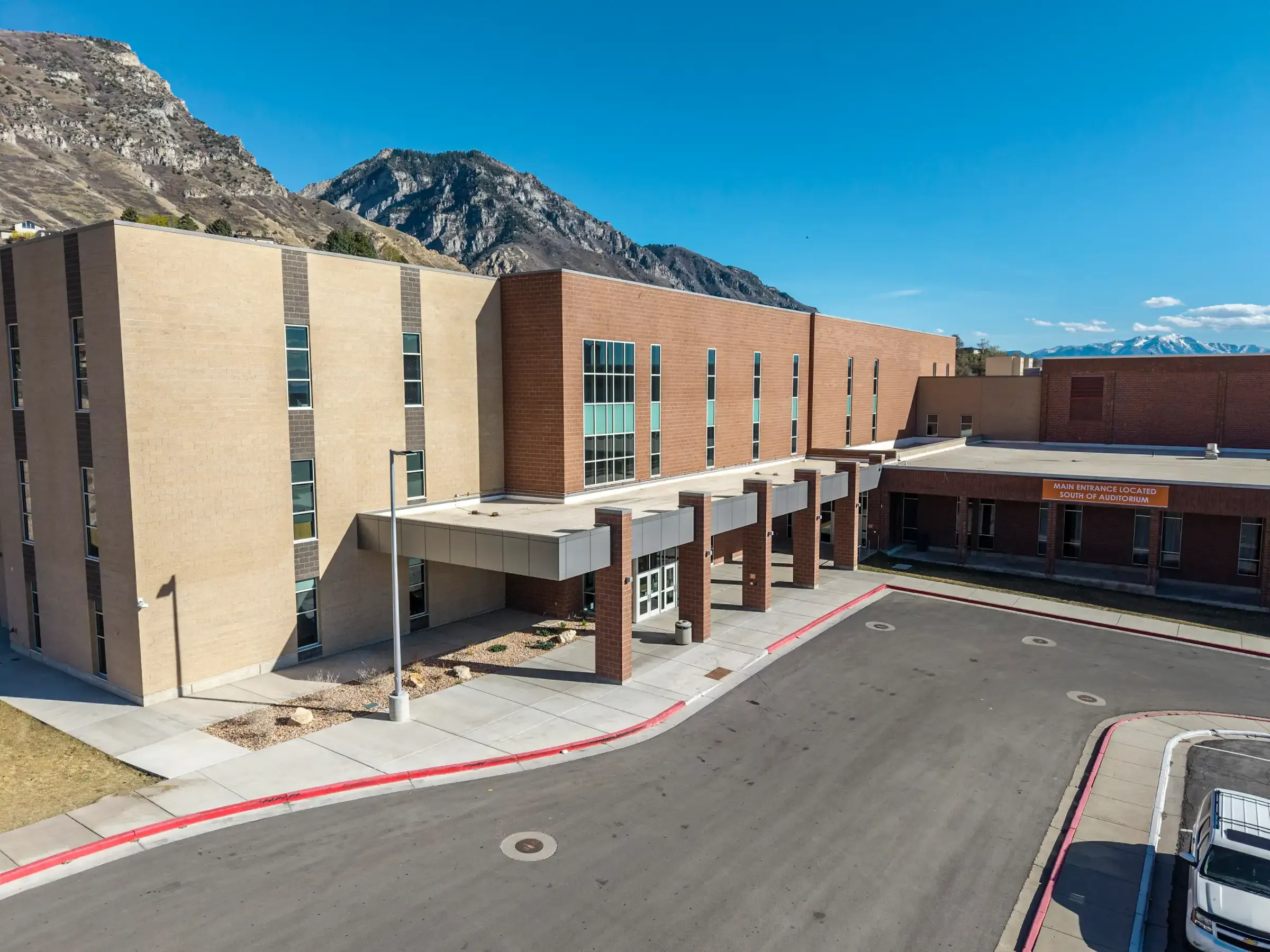 Front entrance of Timpview High School with a brick canopy and tan walls, with rocky mountains rising behind the building.