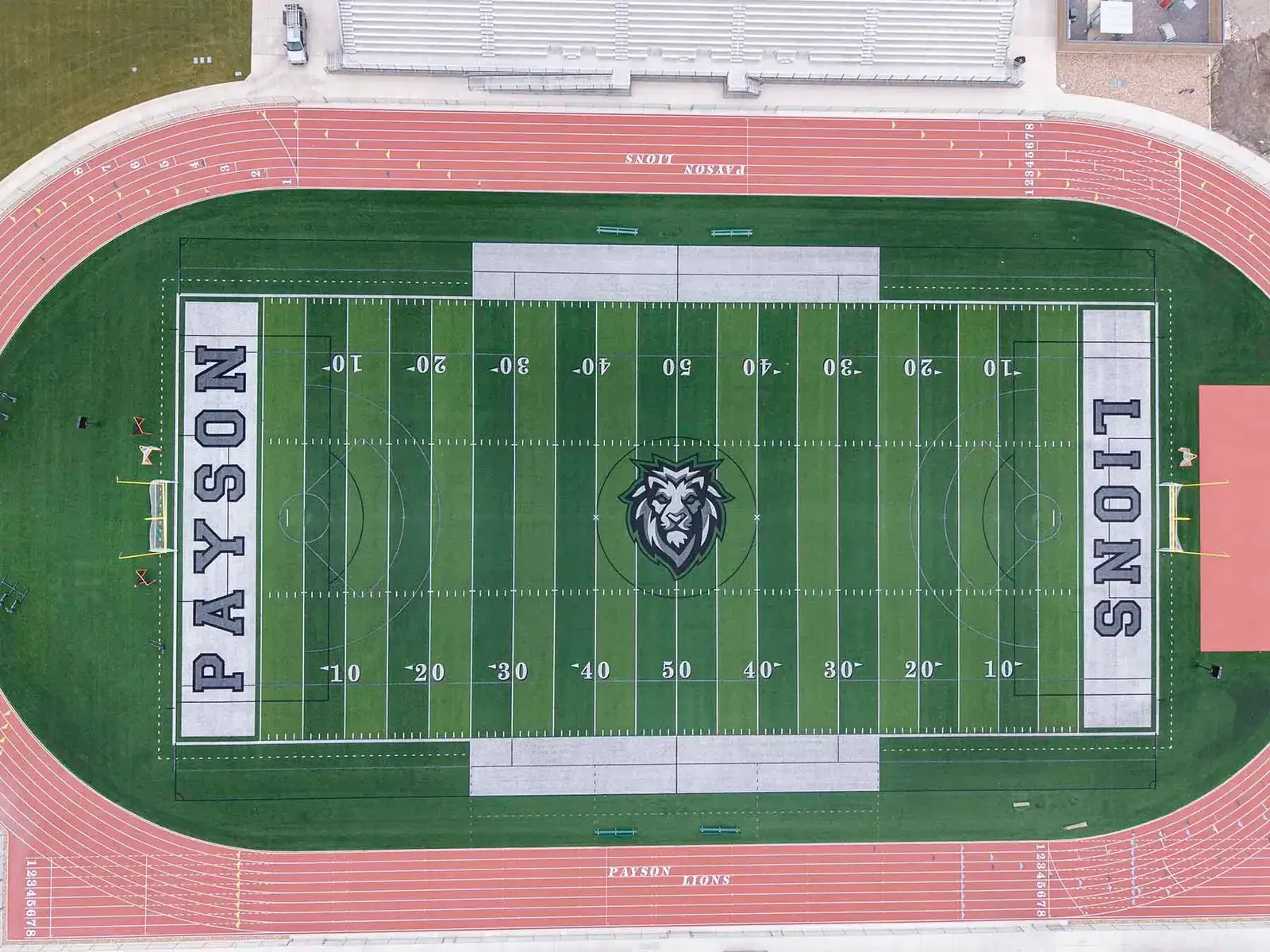 Overhead view of the football field with a lion logo at midfield, PAYSON and LIONS end zones and a red track around it