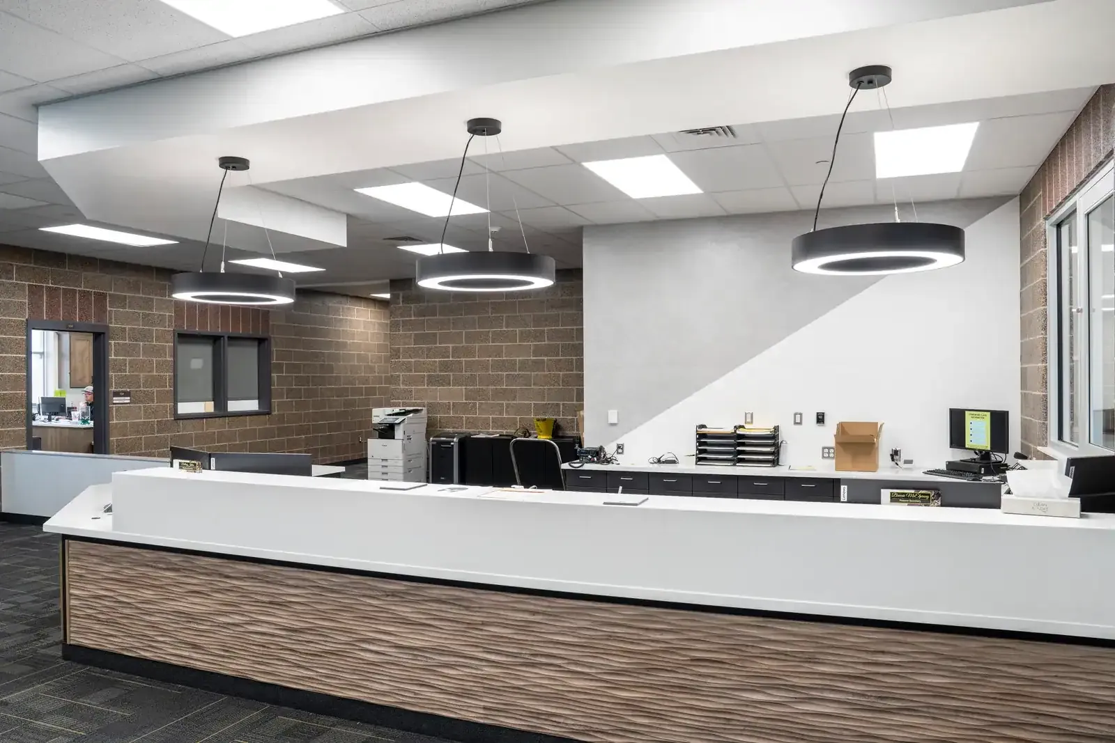 Administration counter with a wood-grain front panel, round pendant lights and an office behind it.