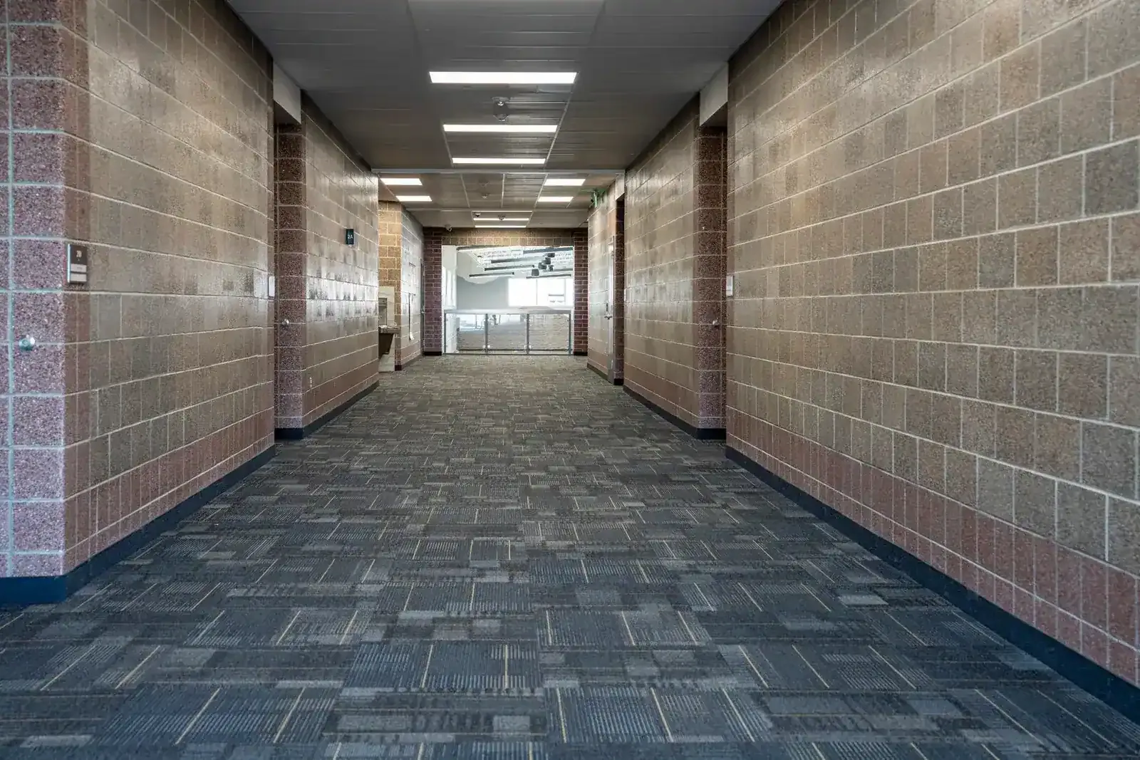 Corridor with pink and tan block walls and patterned gray carpet running toward a glass wall.