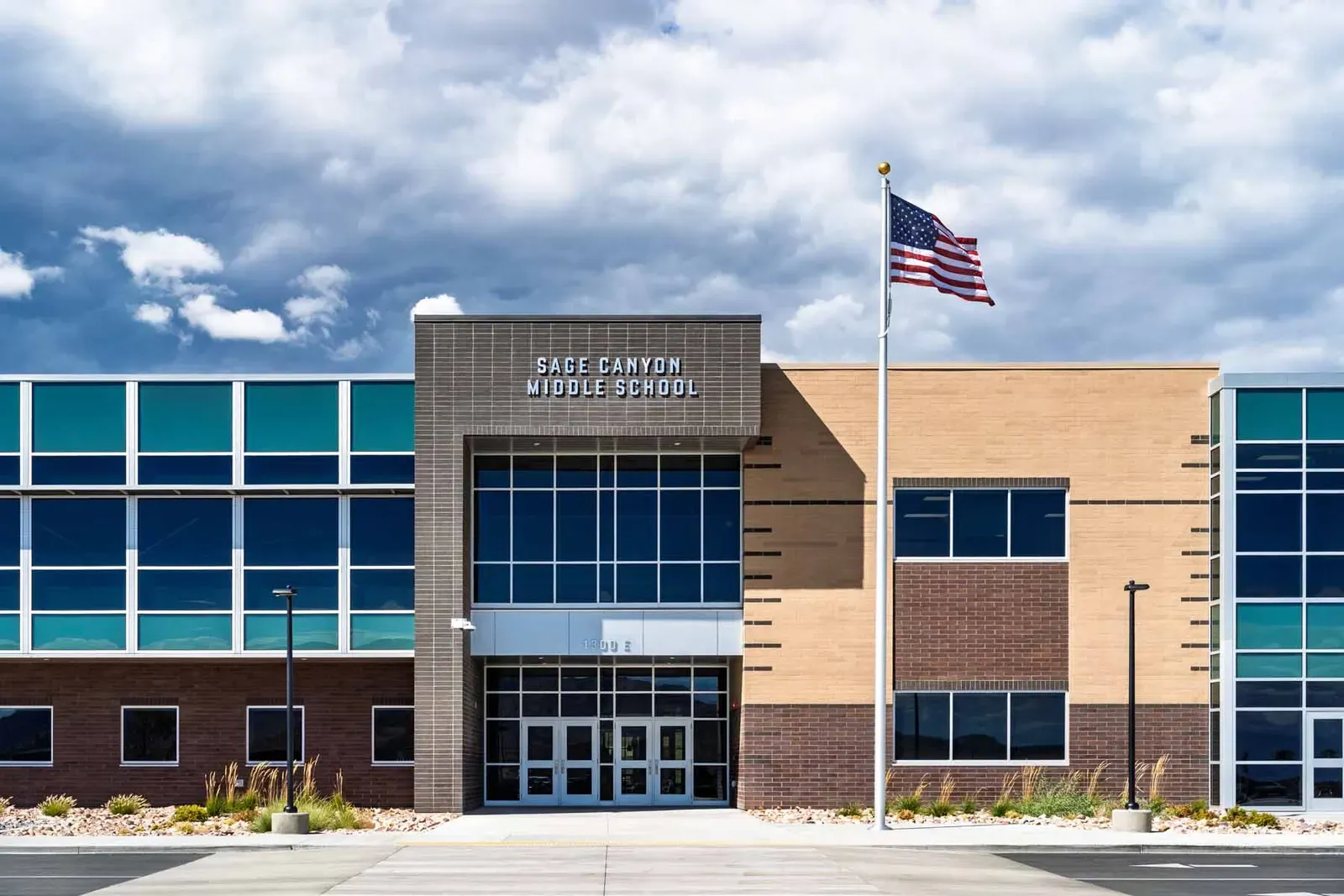 Front of the school with the Sage Canyon Middle School sign, a flagpole and teal glass panels.
