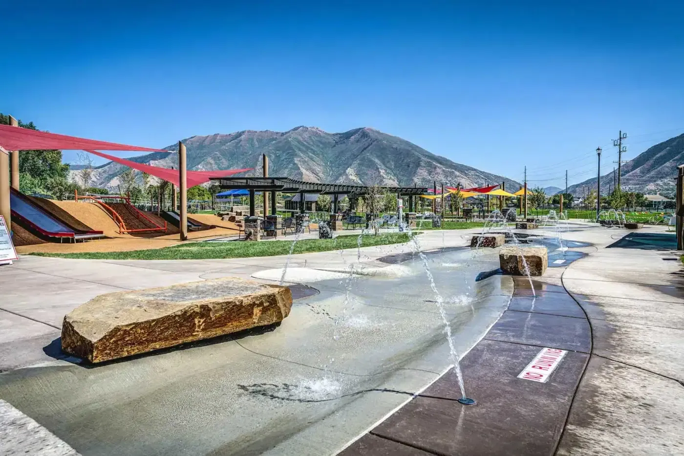 Splash pad with large boulders and shade sails, with mountains in the distance