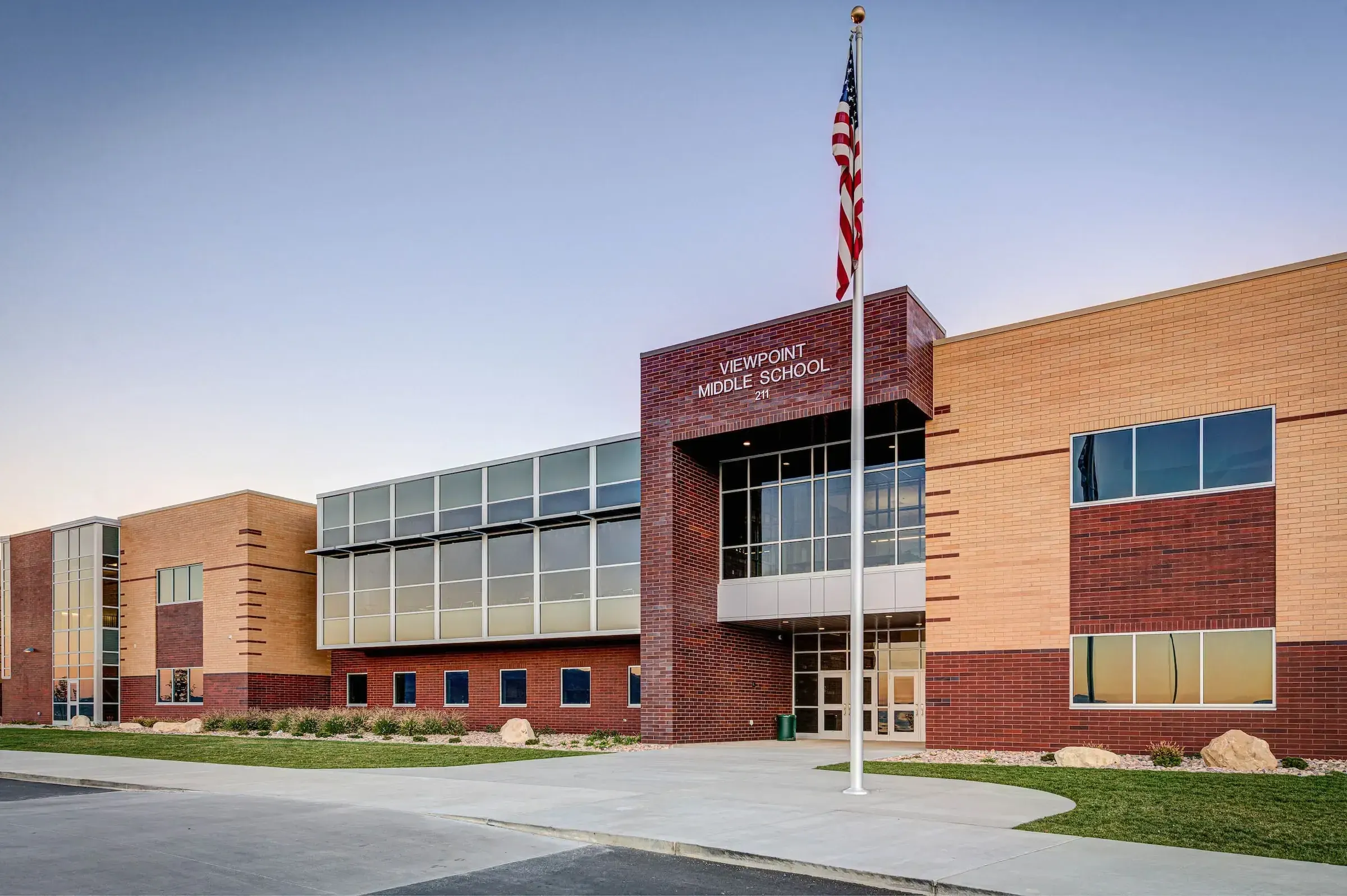 Front of Viewpoint Middle School with a tall brick entrance tower, a flagpole, and tan and red brick wings at dusk.