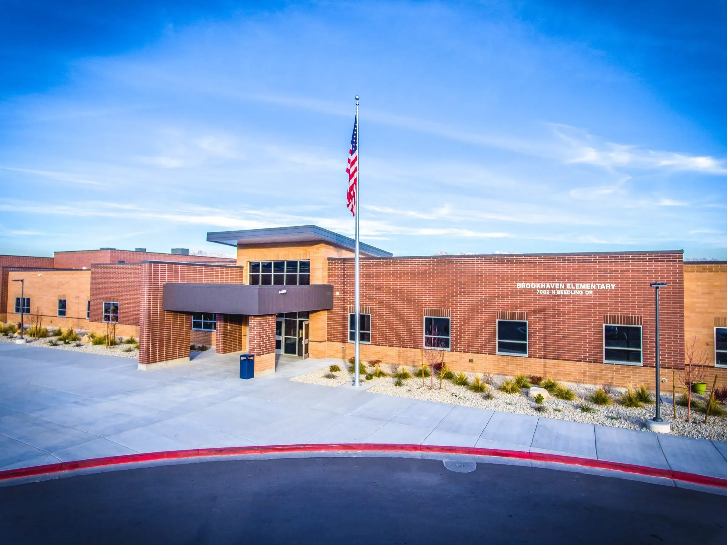 Brick elementary school entrance with a flagpole and a canopy over the doors, under a blue sky