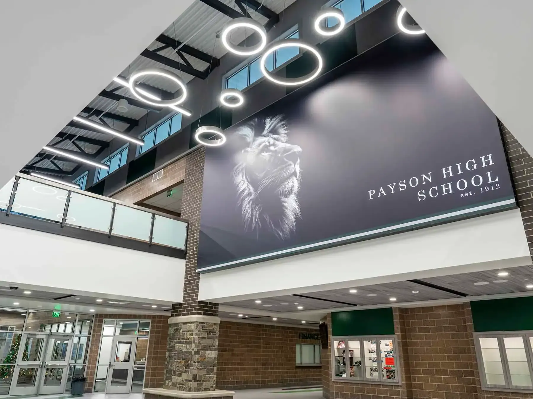 Atrium with a large Payson High School lion banner above brick and stone walls and ring-shaped light fixtures