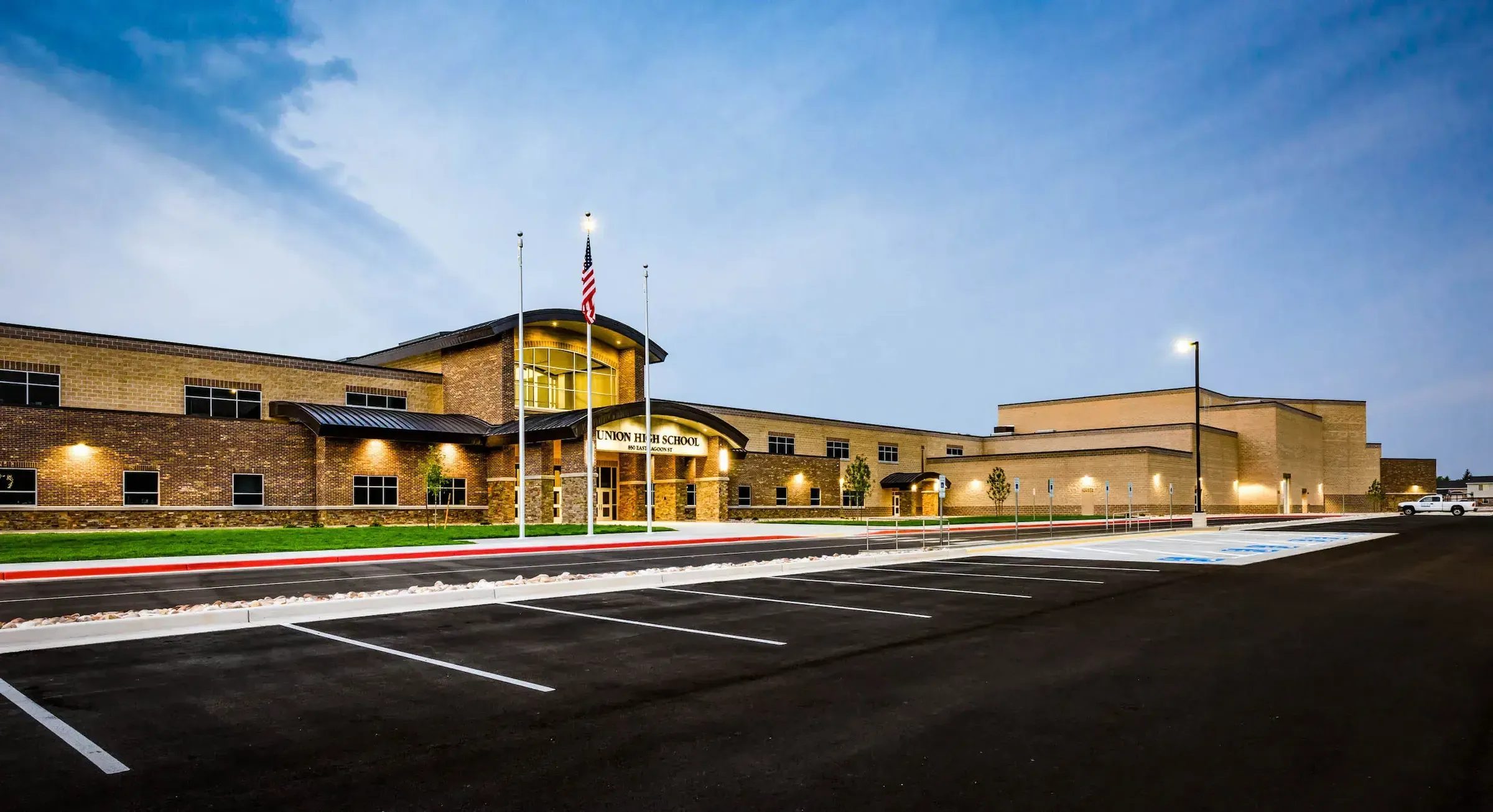 Front of Union High School at dusk with a brick entrance, flagpoles and a large parking lot.