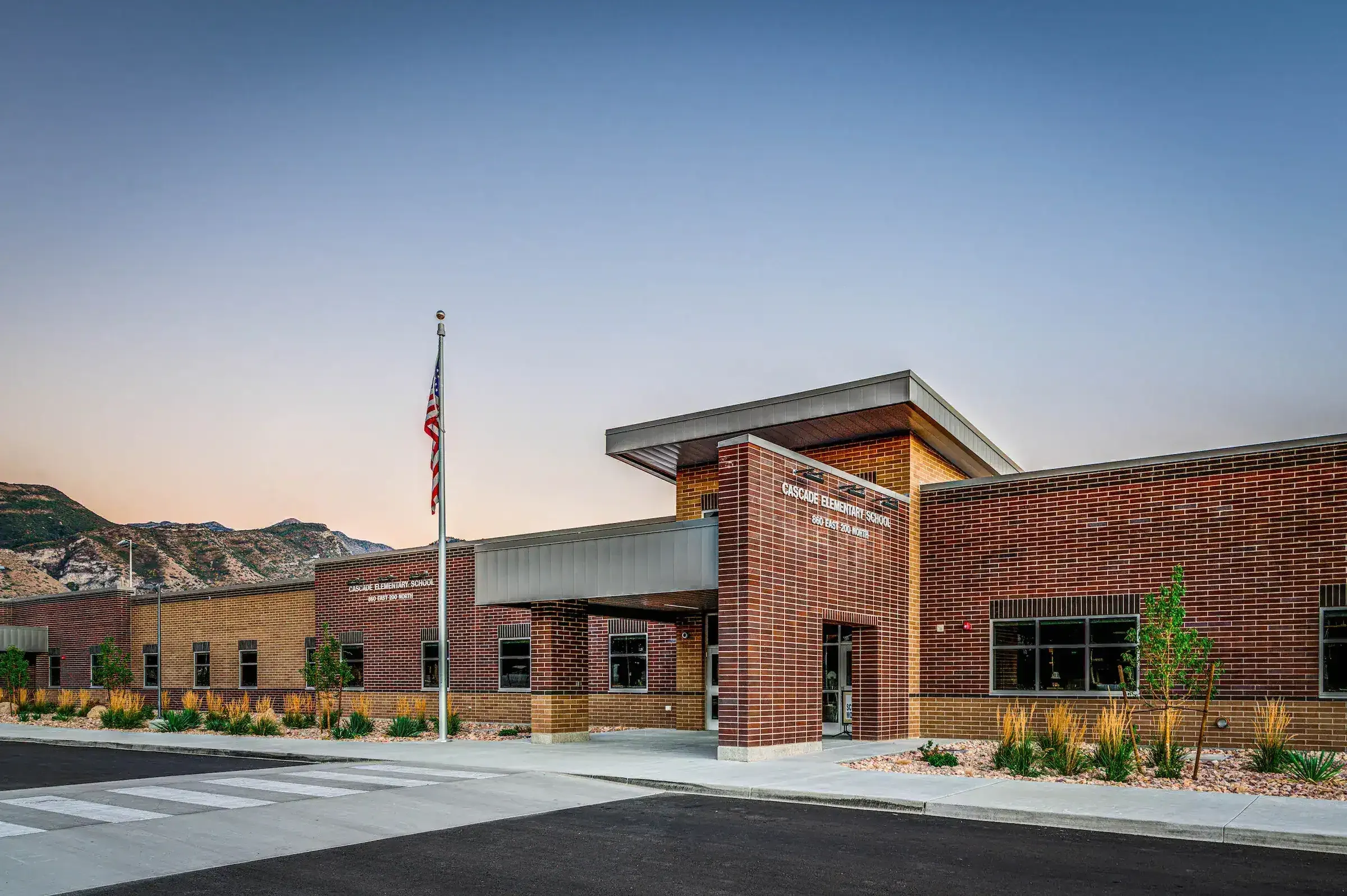 Brick front entrance of the school at dusk with a flagpole and mountains behind.