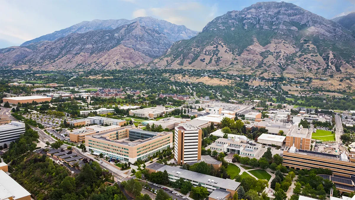 Aerial view of a university campus of tan and white buildings at the foot of steep mountains