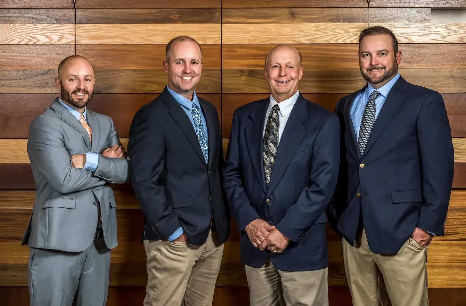 Four men in sport coats smiling in front of a wood-plank wall