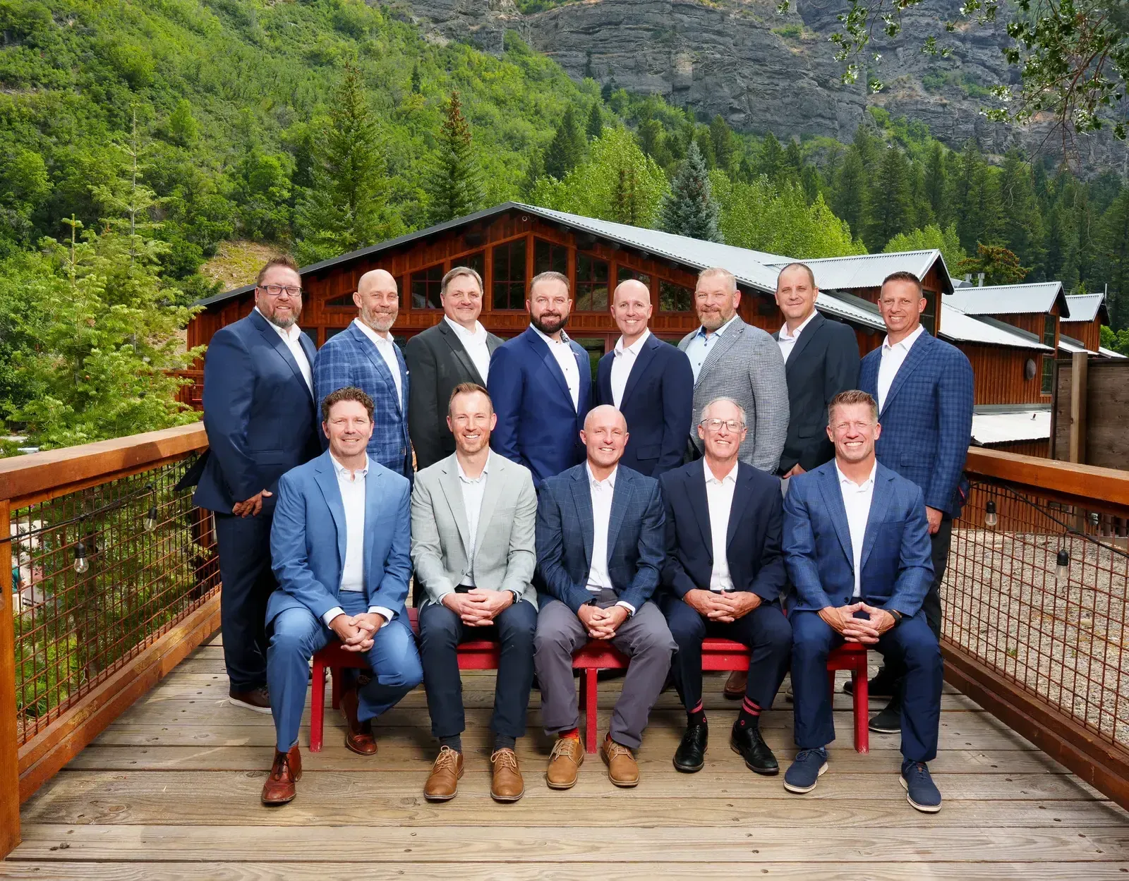 The Westland team in suits, seated and standing on a wooden deck in front of a mountain lodge