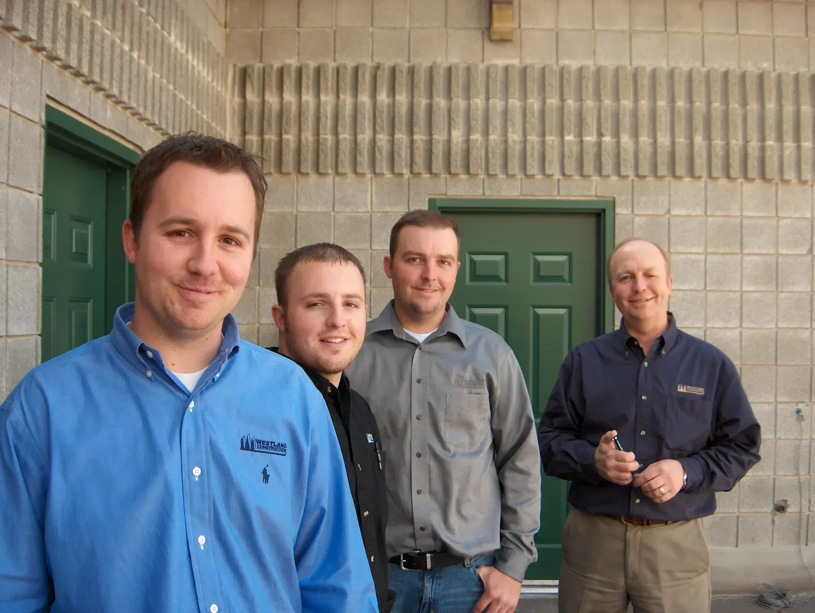 Four Westland team members in work shirts outside a block building with green doors