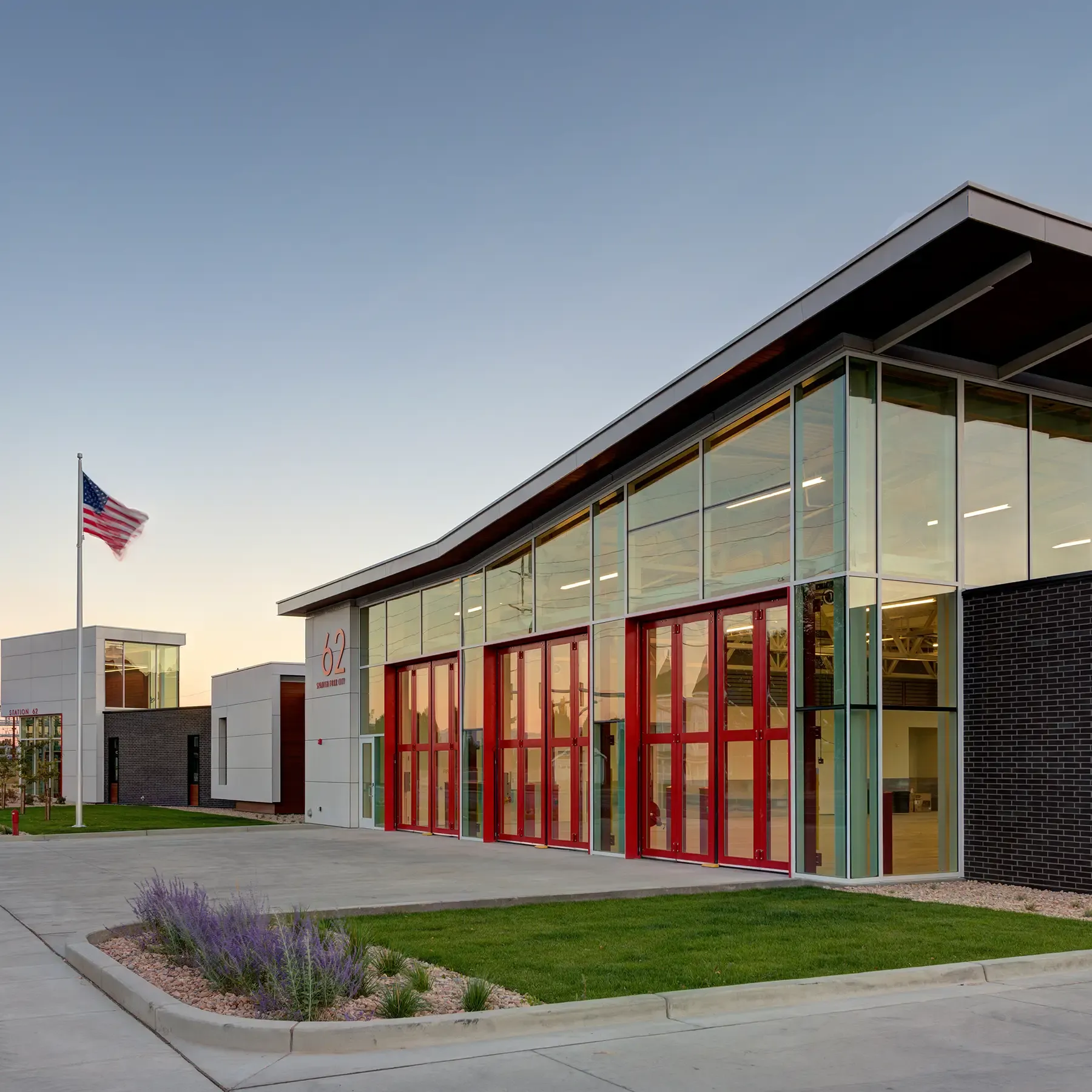 Civic building with red-framed glass bay doors and a flagpole at dusk