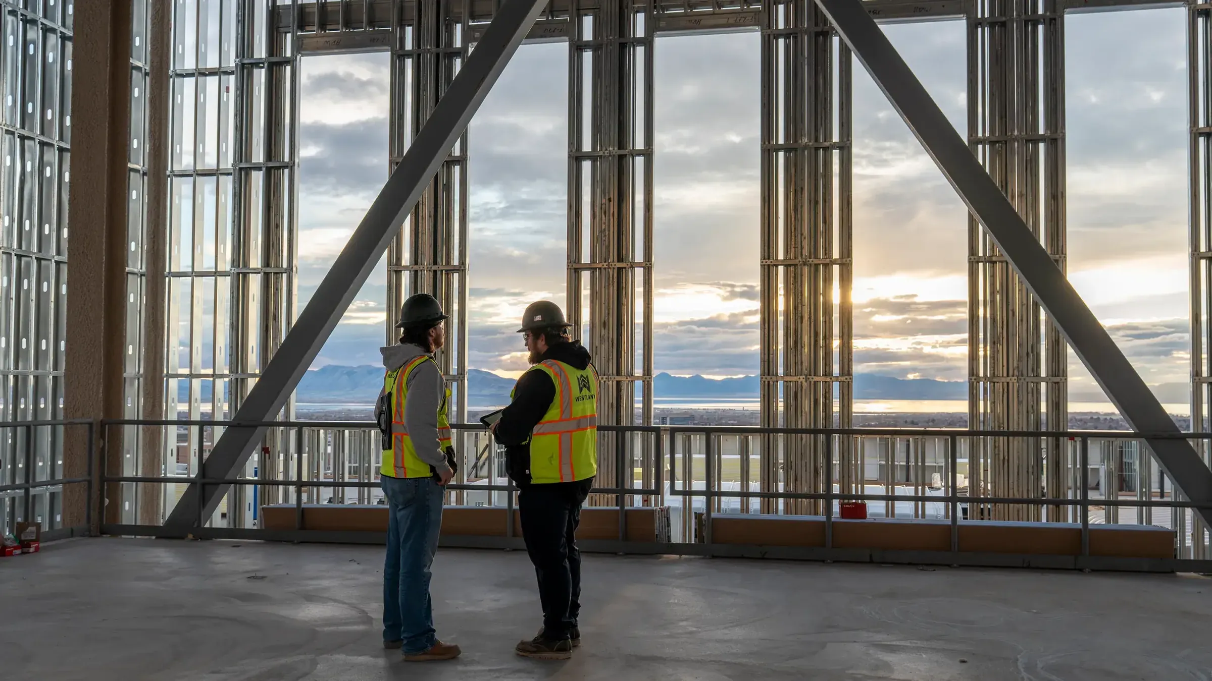 Two Westland team members in safety vests on an open floor of a steel-framed building at sunset